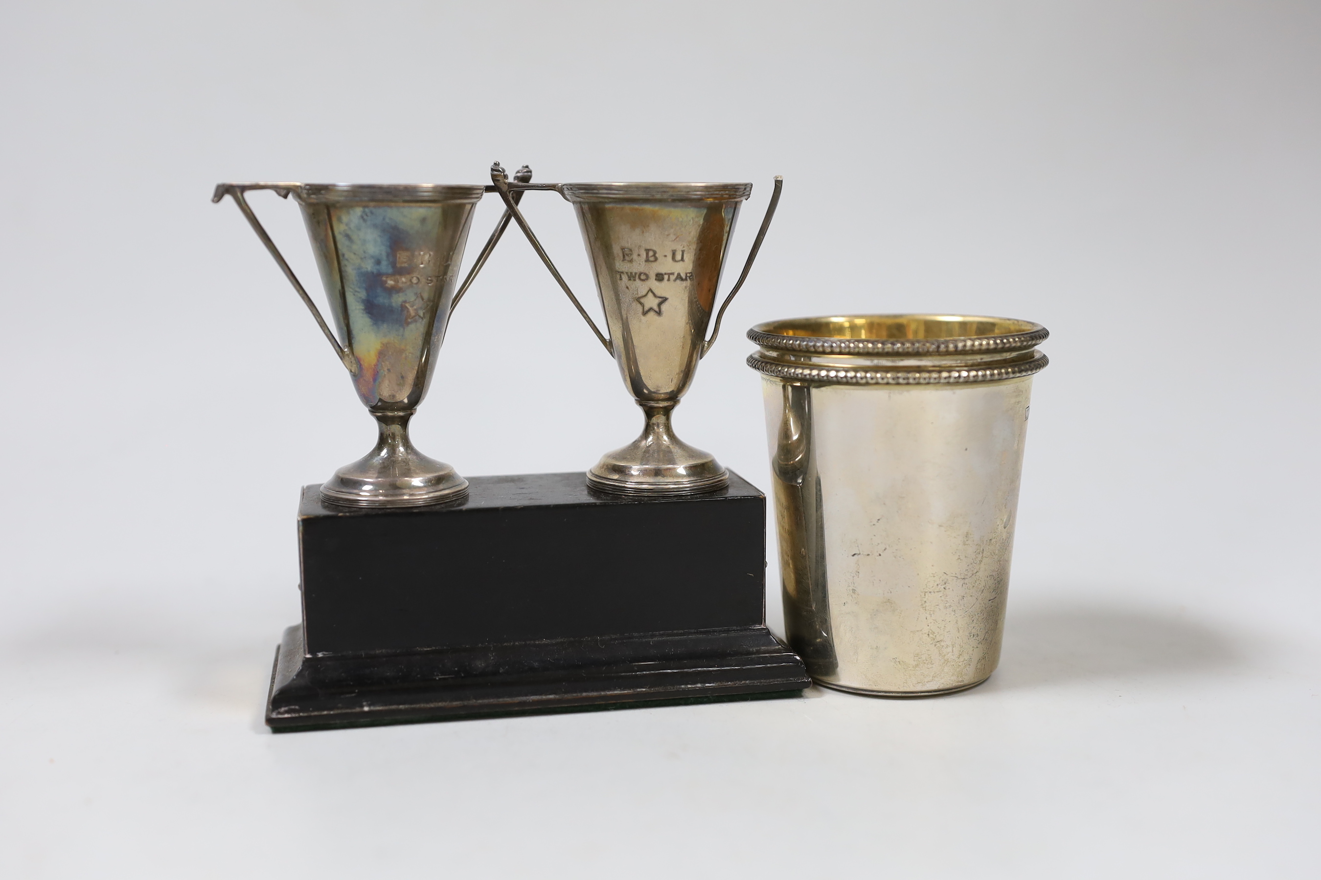 A pair of small silver beakers with gilt interiors and leaded rims, WW, London, 2000, 70mm, two small trophy cups on plinth and a knife in leather scabbard., NB: From the Estate of Rt Hon Lord Lawson of Blaby